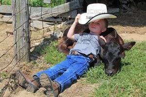 Boy with a cowboy hat laying on a calf